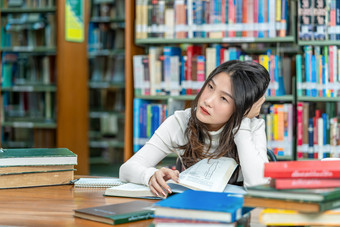 亚洲年轻的学生休闲西装阅读的木表格与各种各样的书图书馆大学通知书的在的书架子上回来学校概念