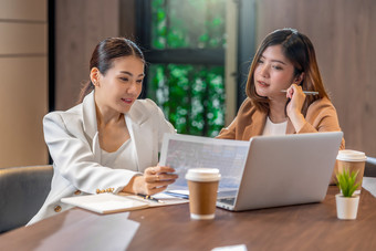 两个亚洲女商人工作与的合作伙伴业务与纸图文档和技术移动PC现代会议房间办公室工作空间咖啡打破合作伙伴和的同事概念
