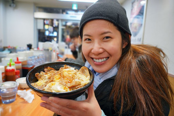 亚洲年轻的女人享受与日本食物哪一个有大米与牛肉烧烤温泉蛋和奶酪的碗鱼市场东京日本