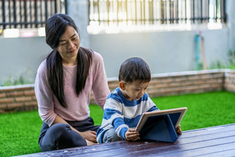 亚洲家庭与儿子是看的卡通通过技术平板电脑和玩在一起当生活前面草坪上为自<strong>我学</strong>习首页学校家庭首页学校概念