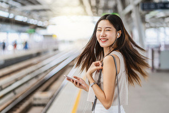 年轻的亚洲女人乘客听音乐通过聪明的移动电话与幸福行动地铁火车站日本中国人朝鲜文生活方式通勤和运输概念