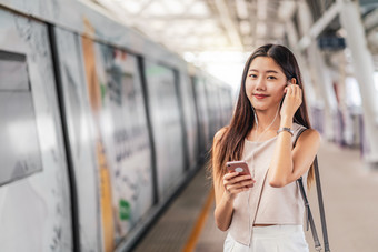 年轻的亚洲女人乘客使用和听音乐通过聪明的移动电话地铁火车站日本中国人朝鲜文生活方式休闲和每天生活通勤和运输概念