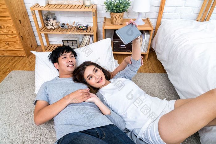 前视图快乐亚洲情人使用的技术聪明的电话为自拍的地板上与地毯卧室首页夫妇自拍概念