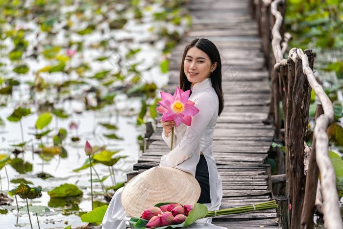 肖像美丽的越南女人与传统的越南他持有的粉红色的莲花坐着的木桥大莲花湖越南爱山东南亚洲旅行概念