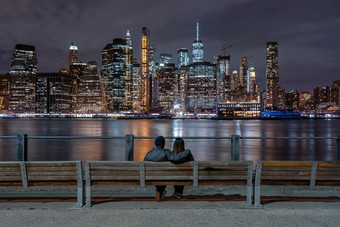场景回来一边夫妇坐着和看新纽约城市景观旁边的东河的晚上时间美国市中心天际线体系结构和建筑与情人概念
