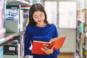 亚洲年轻的学生休闲西装站和阅读的书书架子上图书馆大学通知书的与各种各样的书背景回来学校概念