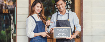 横幅亚洲合作伙伴小业务老板手持有和显示的黑板与欢迎开放标志前面咖啡商店启动与咖啡馆商店安装开放和关闭标签概念