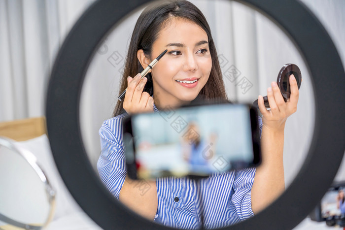 魅力亚洲女人美博主视频博客显示使与调色板和生活社会网络媒体通过视频移动电话视频记录自己化妆教程化妆品视频博客概念