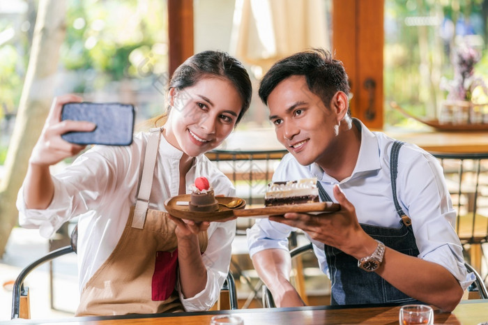 夫妇亚洲两个合作伙伴小业务老板采取自拍和展示的面包店咖啡商店当reccord视频博客蛋糕和甜点企业家博主和启动业务概念