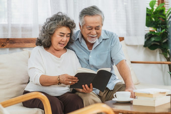 亚洲夫妇祖父母坐着和阅读的书在一起与快乐感觉房子长生活和上了年纪的社会温暖的家庭和幸福科维德爆发和社会距离概念