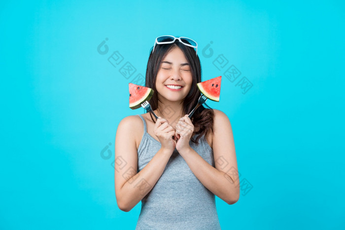 肖像有吸引力的亚洲年轻的女人持有两个一块幻灯片西瓜和穿时尚太阳镜孤立的蓝色的颜色背景复制空间和工作室饮食和健康的水果概念