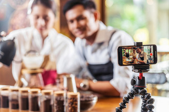 移动电话采取视频两个亚洲咖啡师展示杯咖啡滴咖啡显示观众咖啡商店使表示和美国小业务老板和启动概念