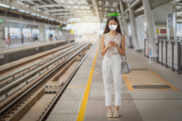 年轻的亚洲女人乘客穿外科手术面具和使用社会网络通过聪明的移动电话地铁火车当旅行大城市通勤和运输与新冠病毒爆发概念