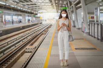 年轻的亚洲女人乘客穿外科手术面具和使用社会网络通过聪明的移动<strong>电话地铁</strong>火车当旅行大城市通勤和运输与新冠病毒爆发概念