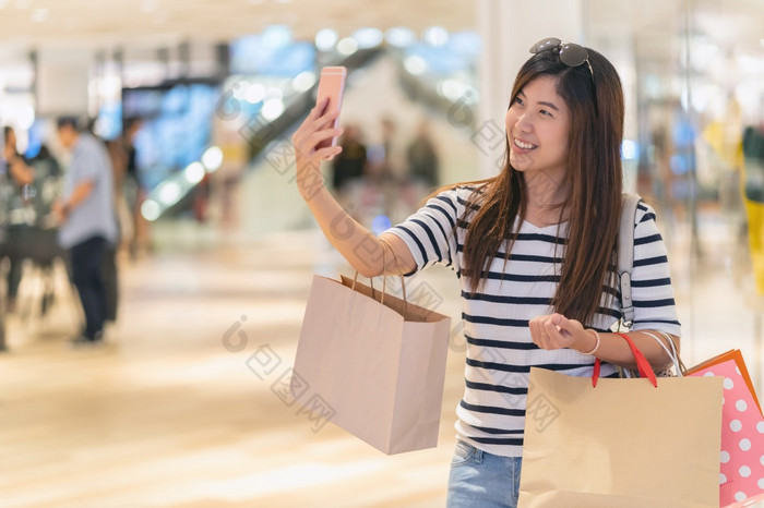 亚洲女人走和使用的聪明的移动电话自拍与模型显示模型与衣服通过的眼镜商店商店与快乐行动部门中心