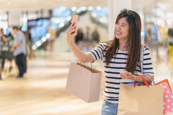 亚洲女人走和使用的聪明的移动电话自拍与模型显示模型与衣服通过的眼镜商店商店与快乐行动部门中心