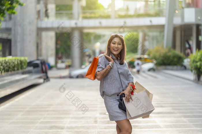 肖像快乐亚洲女人走和持有的购物袋市中心周围购物中心时尚概念