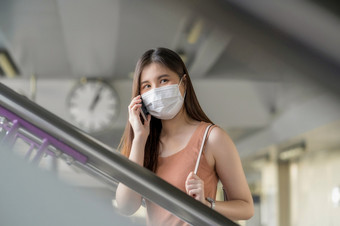 年轻的亚洲女人乘客穿外科手术面具和使用移动电话为会说话的当走的楼梯地铁站而旅行科维德爆发感染和流感大流行概念