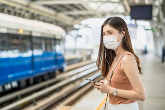 年轻的亚洲女人乘客穿外科手术面具和听音乐通过聪明的移动<strong>电话地铁</strong>火车当旅行大城市科维德爆发感染和流感大流行概念