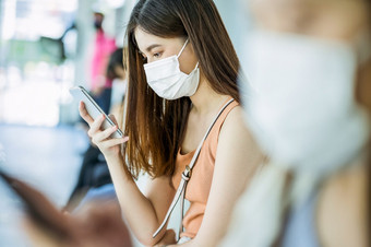 年轻的亚洲女人乘客穿外科手术面具和使用移动电话为社会<strong>网络</strong>当等待公共汽车站与加冕人当旅行大城市科维德爆发感染和流感大<strong>流行</strong>概念