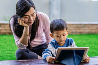 亚洲家庭与儿子是看的卡通通过技术平板电脑和玩在一起当生活前面草坪上为自我学习首页学校家庭首页学校概念