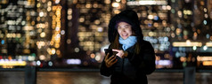 横幅和封面亚洲女人冬天西装使用聪明的移动电话与微笑行动在的照片模糊散景新纽约城市景观旁边的东河背景美国市中心