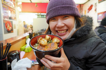 亚洲年轻的女人享受与日本食物哪一个<strong>有大米</strong>与鳗鱼咕噜咕噜和扇贝的碗鱼市场东京日本