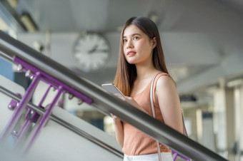 年轻的亚洲女人乘客穿耳机和使用聪明的移动电话和走的楼梯地铁站当旅行大城市通勤和运输概念