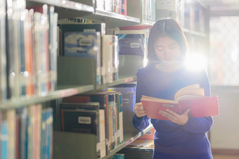 亚洲年轻的学生休闲西装站和阅读的书书架子上图书馆大学通知书的与各种各样的书背景回来学校概念