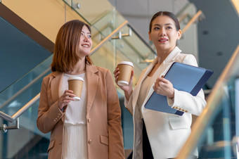 两个亚洲女商人走和会说话的在咖啡打破现代办公室共同办公空间咖啡打破放松和会说话的后工作时间业务和人伙伴关系概念