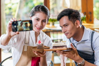 夫妇亚洲两个合作伙伴小业务老板采取自拍和展示的面包店咖啡商店当reccord视频博客蛋糕和甜点企业家博主和启动业务概念