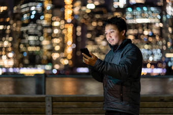亚洲男人。穿大衣西装使用聪明的移动电话与微笑行动在的照片模糊散景新纽约城市景观旁边的东河美国市中心职业生涯工作到处都是概念