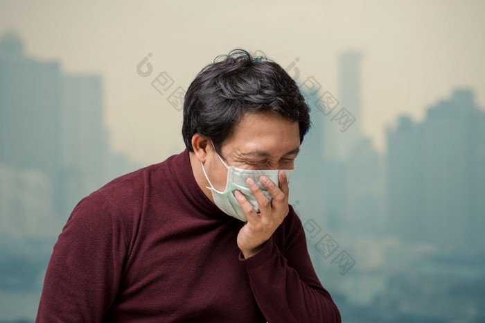 亚洲男人。穿的脸面具对空气污染与咳嗽的阳台高公寓哪一个可以看到污染和重雾在的曼谷城市景观背景医疗保健概念