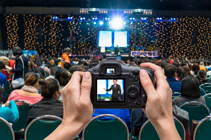 手持有的相机采取照片的商人的阶段在的后视图观众的会议大厅展览中心背景业务会议和教育概念