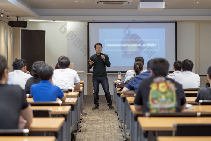 亚洲演讲者与休闲西装的阶段前面的房间与低光在的演讲屏幕的业务教育研讨会业务和教育概念