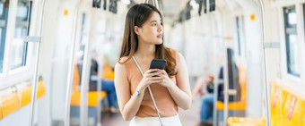 年轻的亚洲女人乘客使用聪明的移动电话和看外地铁火车当旅行大城市通勤和运输概念