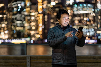 亚洲男人。穿大衣西装使用聪明的移动电话与微笑行动在的照片模糊散景新纽约城市景观旁边的东河美国市中心职业生涯工作<strong>到处都是</strong>概念