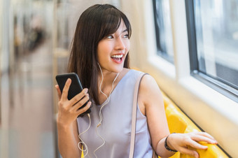 年轻的亚洲女人乘客听音乐通过聪明的移动<strong>电话地铁</strong>火车当旅行大城市日本中国人朝鲜文生活方式和每天生活通勤和运输概念