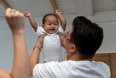 亚洲父亲持有的男孩婴儿提高手和妈妈。手的房子家庭生活方式概念