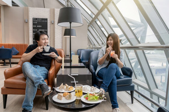 亚洲夫妇坐着和食在机场休息室当等待的飞行现代国际机场旅行和运输概念