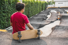 亚洲男人。坐着与surfskate滑冰董事会pumptrack滑冰公园当日出时间在照片模糊pumptrack曲线extream体育运动健康的和锻炼时尚科维德概念