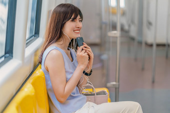 年轻的亚洲女人乘客听音乐通过聪明的移动电话地铁火车当旅行大城市日本中国人朝鲜文生活方式和每天生活通勤和运输概念