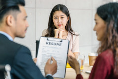 年轻的亚洲女人研究生面试与两个经理当讨论关于她的重新开始与严重的运动会议房间业务招聘新成员概念