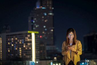 亚洲女商人使用聪明的移动电话与微笑行动的金融区区域曼谷河一边泰国技术与职业生涯概念