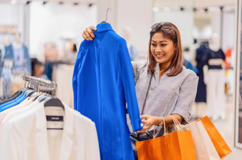 快乐亚洲女人选择衣服玻璃商店商店与快乐行动部门中心购物和购物狂生活方式时尚和休闲销售和黑色的星期五概念