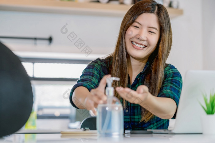亚洲女人使用手洗手液当工作首页与技术移动PC和移动电话厨房房间工作首页新冠病毒流感大流行概念