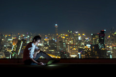 亚洲商人坐着和使用的移动PC在的城市景观背景晚上时间业务成功和技术概念