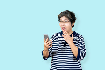 惊讶高级亚洲女人持有和看智能手机孤立的背景感觉惊讶和惊讶老女生活方式概念蓝色的背景