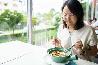 新正常的中年亚洲女人吃食物与塑料板防止的传播的病毒社会距离和和保持距离