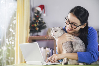 快乐年轻的亚洲女人在线使用移动PC而连接视频调用美丽的女人说话看相机会说话的与她的朋友视频调用和可爱的猫休息首页